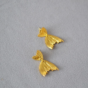 Macro shot of gold fish tail earrings featuring fine radial vertical textures on gray fabric