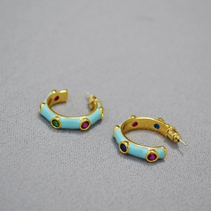 Detail view of gold C-shaped earrings with light blue enamel and colorful zircon stones