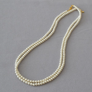 Gros plan d'un collier de perles blanches à double rangée avec fermoir doré en métal