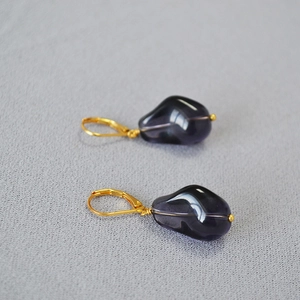 Detail of elegant gold drop earrings with dark translucent pebble charms on soft fabric