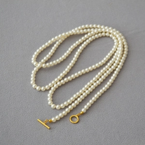 Détail d'un collier de perles blanches multicouches avec fermoir OT doré sur gris