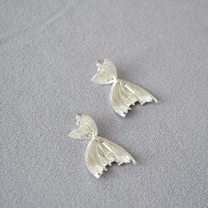 Macro shot of silver fish tail earrings with delicate radial texture on grey fabric
