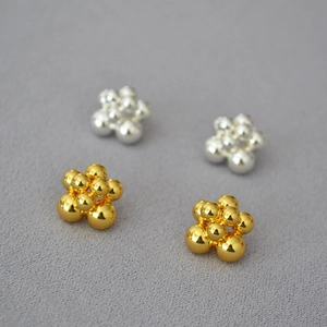 Macro shot of layered gold and silver cluster bead earrings on a grey textured background