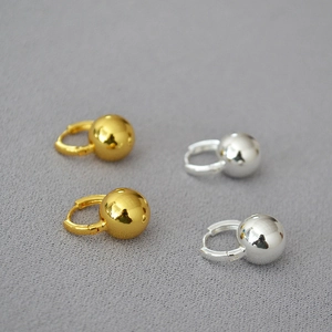 Minimalist gold and silver spherical drop earrings displayed on a grey textured background