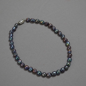 Detailed view of dark peacock green baroque pearls with a silver oval metal clasp