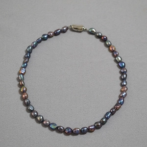 Macro detail of peacock green baroque pearls with metallic cylinder clasp on gray fabric