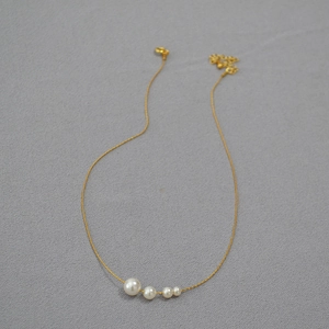 Détail du collier en chaîne fine dorée avec quatre perles blanches dégradées et fermoir