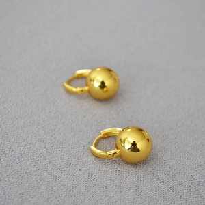 Macro view of gold ball earrings with polished finish on gray textured fabric