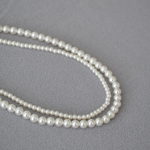 Close-up of dual-layer pearl necklace showing different bead sizes on grey fabric