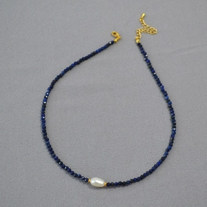 Macro shot of faceted blue spinel beads with a baroque pearl on a gold clasp necklace