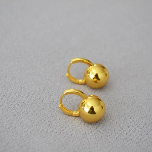 Macro detail of polished gold ball hoop earrings on textured grey fabric background