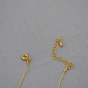 Détail du collier doré montrant le fermoir ressort, la chaînette et le pendentif goutte