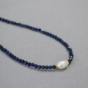 Macro shot of blue lapis lazuli beads with a white baroque pearl on a choker necklace