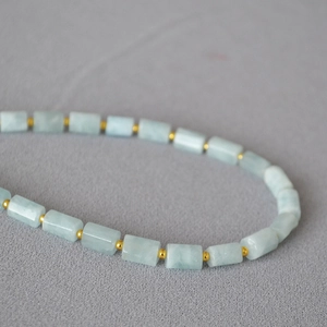 Close-up of handmade necklace with light blue stones and golden metal separator beads