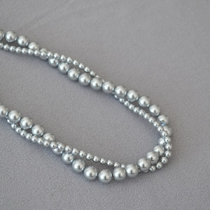 Detail shot of multi-layer faux pearl necklace with silver-grey beads on textured fabric