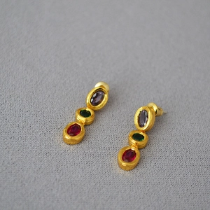Detail of gold-plated drop earrings featuring three colorful oval gems and textured finish