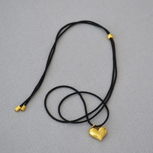 Detailed top view of a gold heart pendant necklace with adjustable black cord on fabric