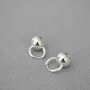 Minimalist silver spherical drop hoop earrings displayed on a soft textured fabric