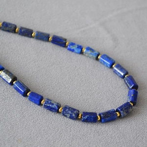 Macro detail of cylindrical blue lapis lazuli beads with gold spacers on stone necklace