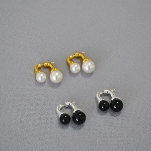 Close-up of U-shaped earrings with white pearls and black beads in gold and silver finish