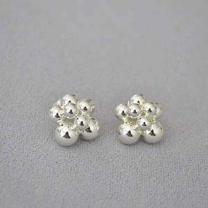 Macro detail of silver floral stud earrings featuring a tiered polished golden bead cluster