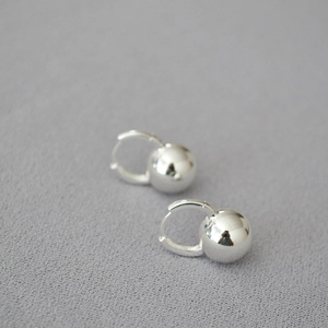 Macro shot of minimalist silver ball hoop earrings on a light grey textured fabric surface
