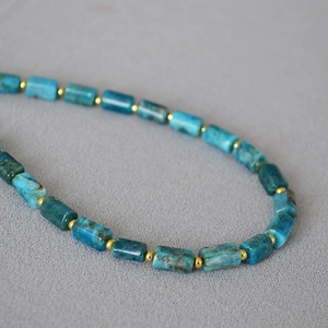 Artisan blue stone cylinder beaded necklace with gold spacers on grey fabric background