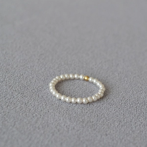 Macro detail of a 14K gold filled bead and delicate white pearls on a minimalist ring
