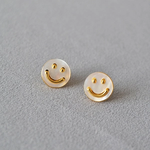Dettaglio di orecchini tondi in madreperla con motivo smiley dorato su base bianca