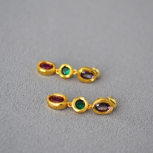 Detail of gold brass earrings with red, green, and purple oval gemstones and silver pins