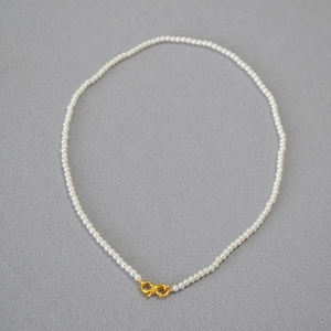 Detail of elegant pearl necklace featuring a golden infinity clasp over grey fabric