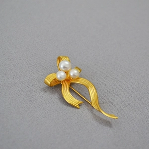 French vintage gold bow brooch with three freshwater pearls on a grey textured background