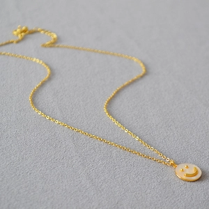 Primo piano dettagliato di una collana dorata con ciondolo a forma di smile in madreperla