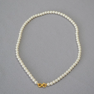 Detail of high-luster round pearls with a gold infinity-shaped clasp on a textured background