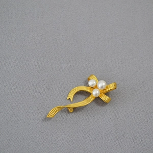 French vintage gold ribbon brooch with freshwater pearls on a grey textured fabric
