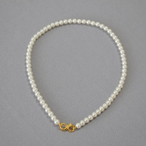 Detail of round faux pearl necklace with golden infinity clasp on grey background