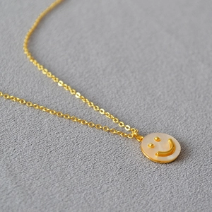 Dettaglio di una collana con ciondolo a faccina sorridente dorata su sfondo grigio