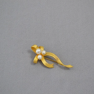 Detail of gold ribbon brooch featuring mesh texture and three elegant freshwater pearls