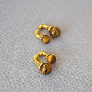 Detailed macro of golden U-shaped stud earrings featuring striped tiger eye gemstones