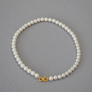 Close-up of elegant white pearl necklace featuring a golden infinity symbol clasp