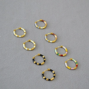 Macro view showing various colorful enamel hoop earrings with gold-plated metal texture