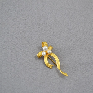 Close-up of gold ribbon brooch with brushed texture and three white pearls