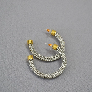 Macro detail of gold-plated C-hoop earrings featuring pavé-set shimmering crystals