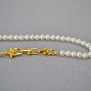 Détail du fermoir en U doré et des perles blanches sur un collier élégant et moderne