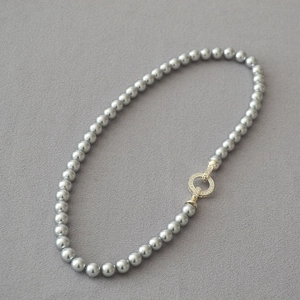 Elegant grey round pearl necklace with a gold micro-pave zircon buckle on felt background