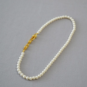 Collier de perles élégant avec maillon en U doré sur fond gris à texture fine