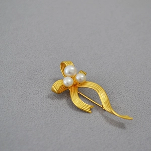 Detailed view of gold ribbon brooch with freshwater pearls and woven texture