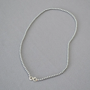 Close-up of minimalist silver beaded necklace with metal lobster clasp on grey fabric