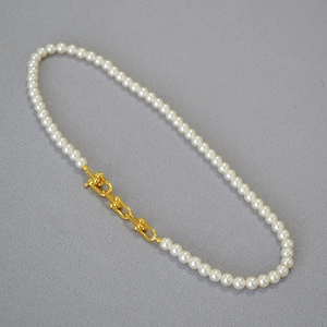 Détail d'un collier de perles avec maillons dorés en U sur fond de textile gris