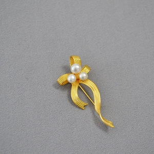 Detailed close-up of golden ribbon bow brooch with three round white pearls on grey fabric